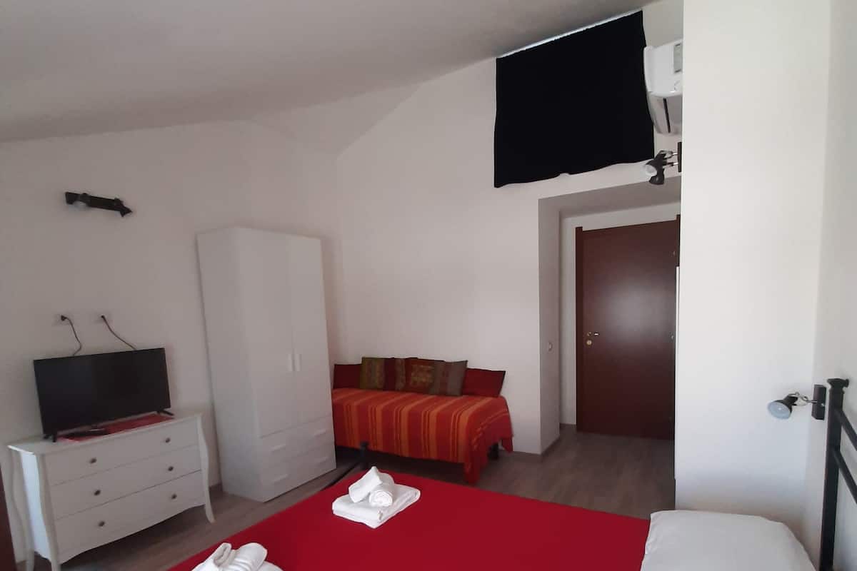 A hotel room with a large bed, a TV mounted on the wall, a wardrobe, and a door leading to another room.