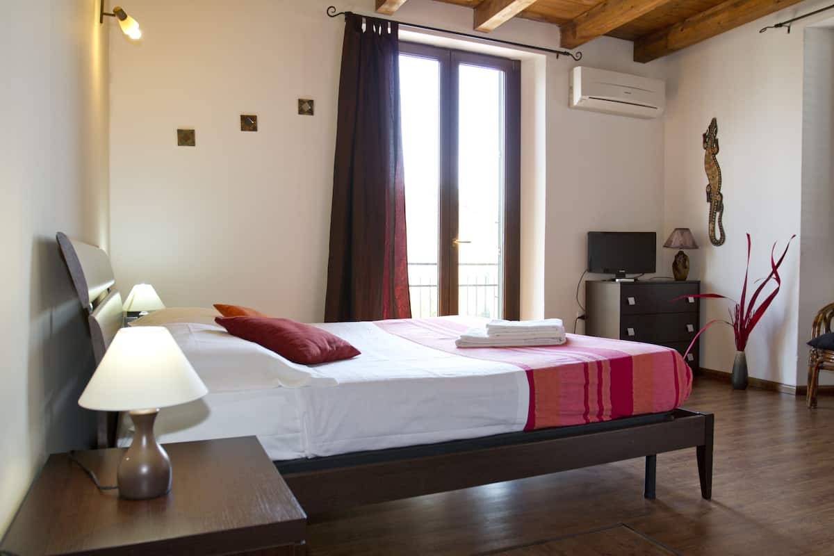 A bedroom with a bed, bedside lamp, TV, dresser, and a window with curtains.