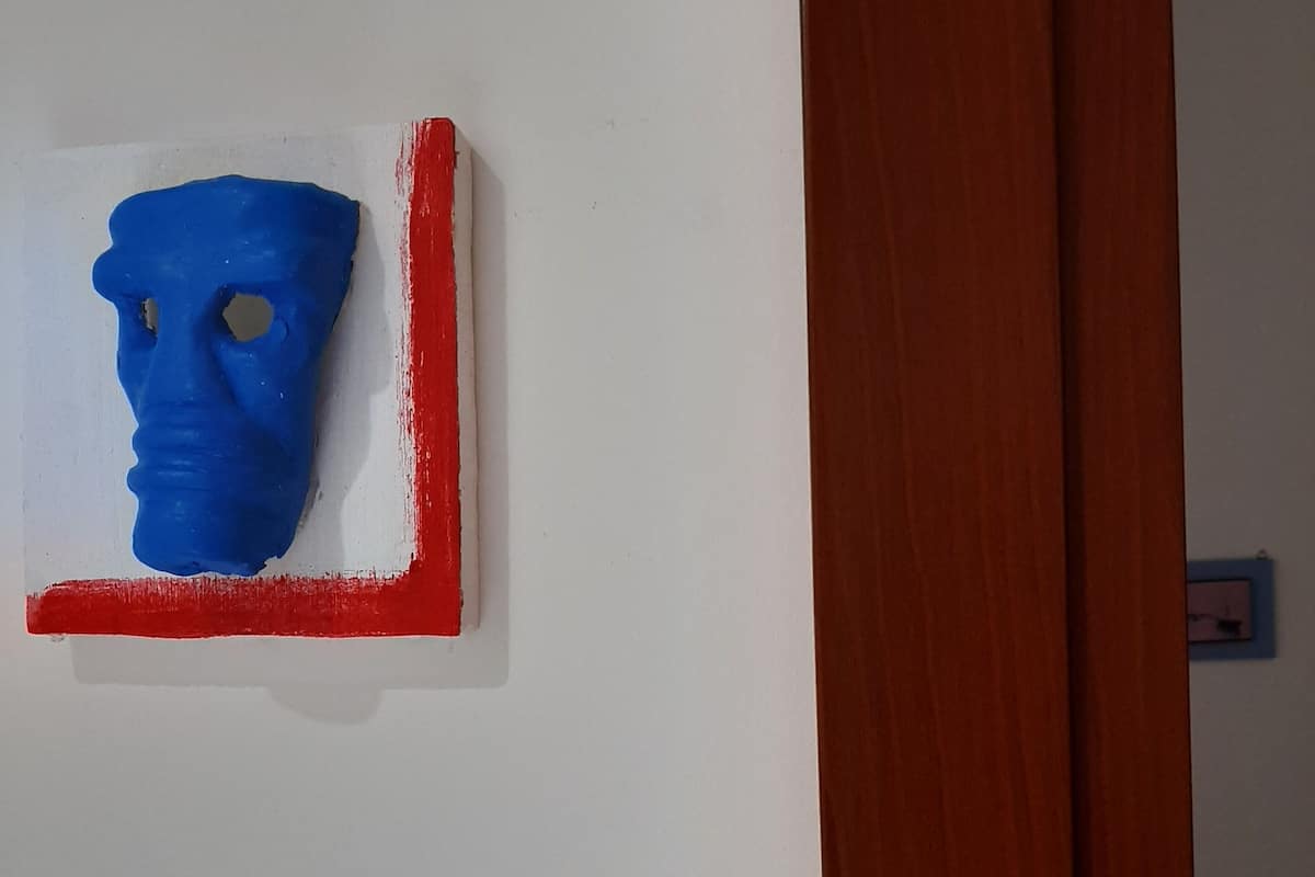 A blue sculpture mounted on a white wall with a red border.