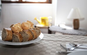 A plate of sliced bread on a table with a checkered tablecloth, accompanied by a fork and spoon. - Cuscino e Cappuccino (Alghero)