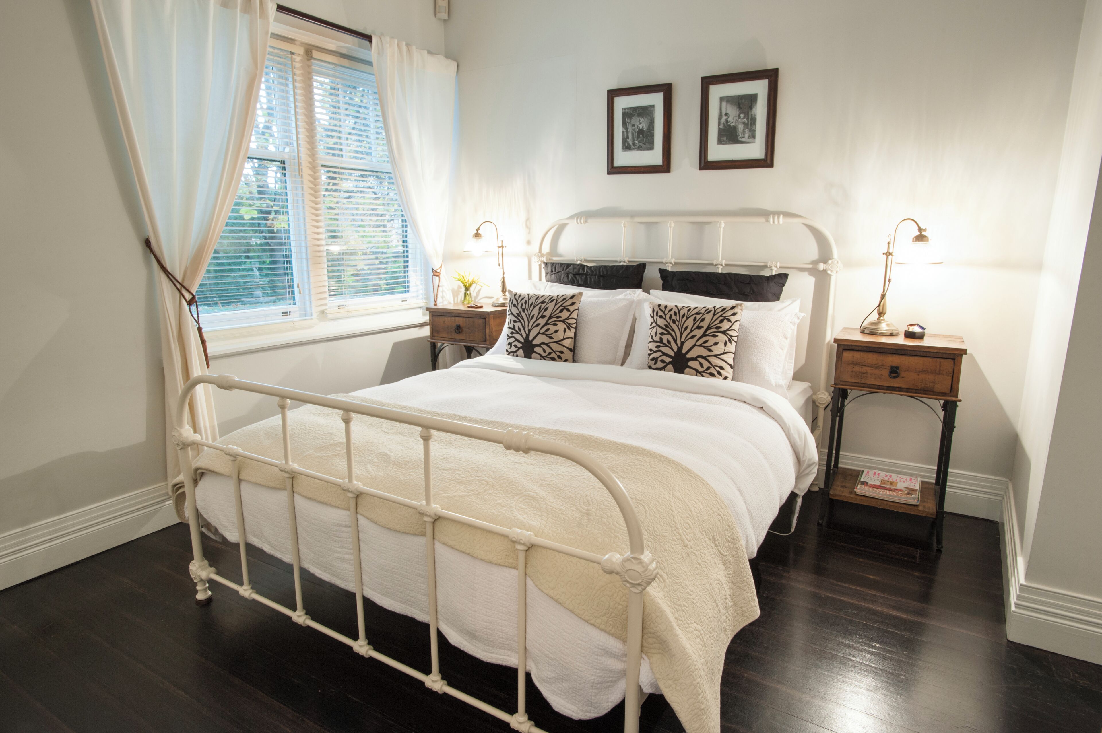 A neatly made bed with a white metal frame, two bedside tables with lamps, and a window with curtains.