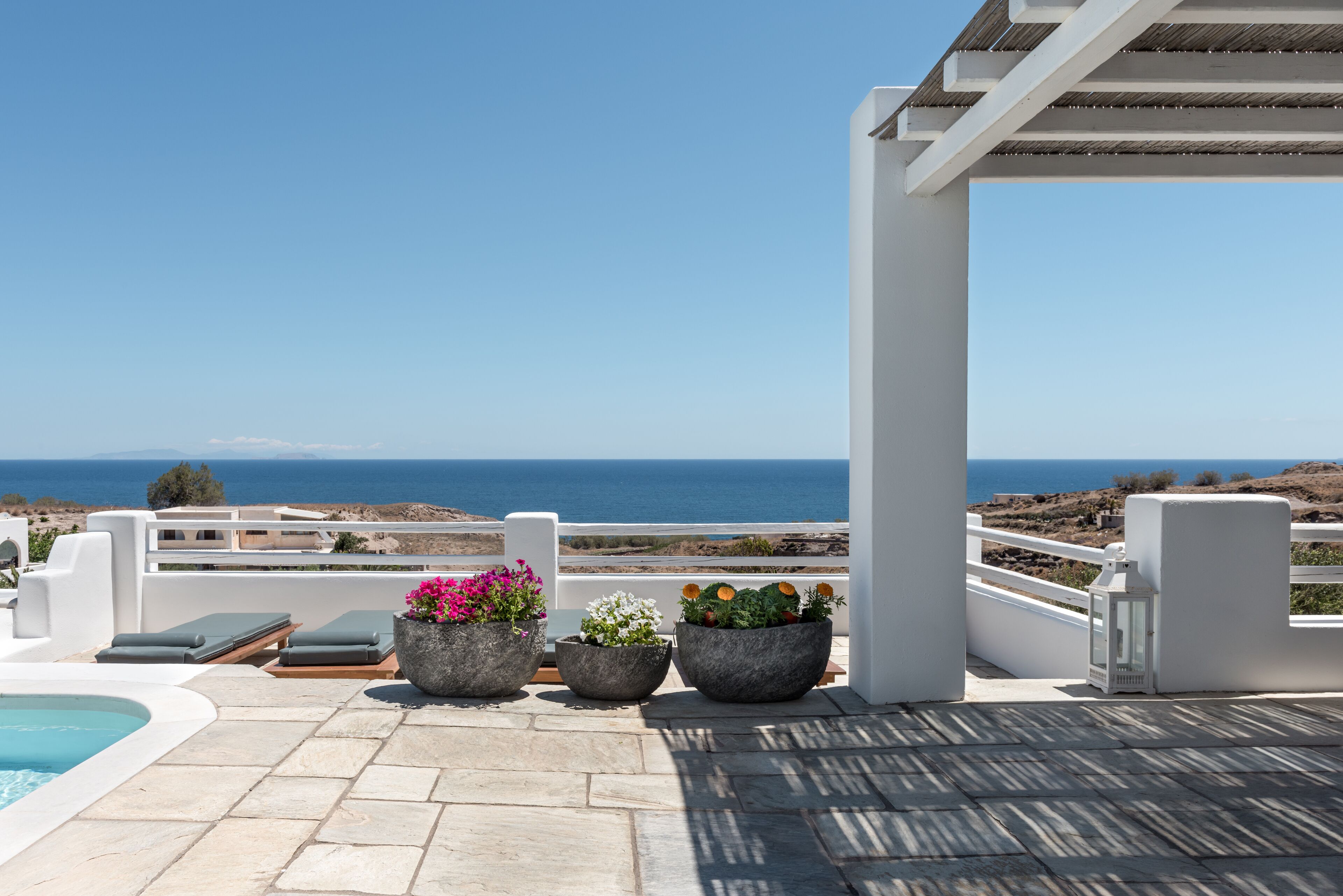 A rooftop terrace with a pool, lounge chairs, and potted plants overlooking the sea.