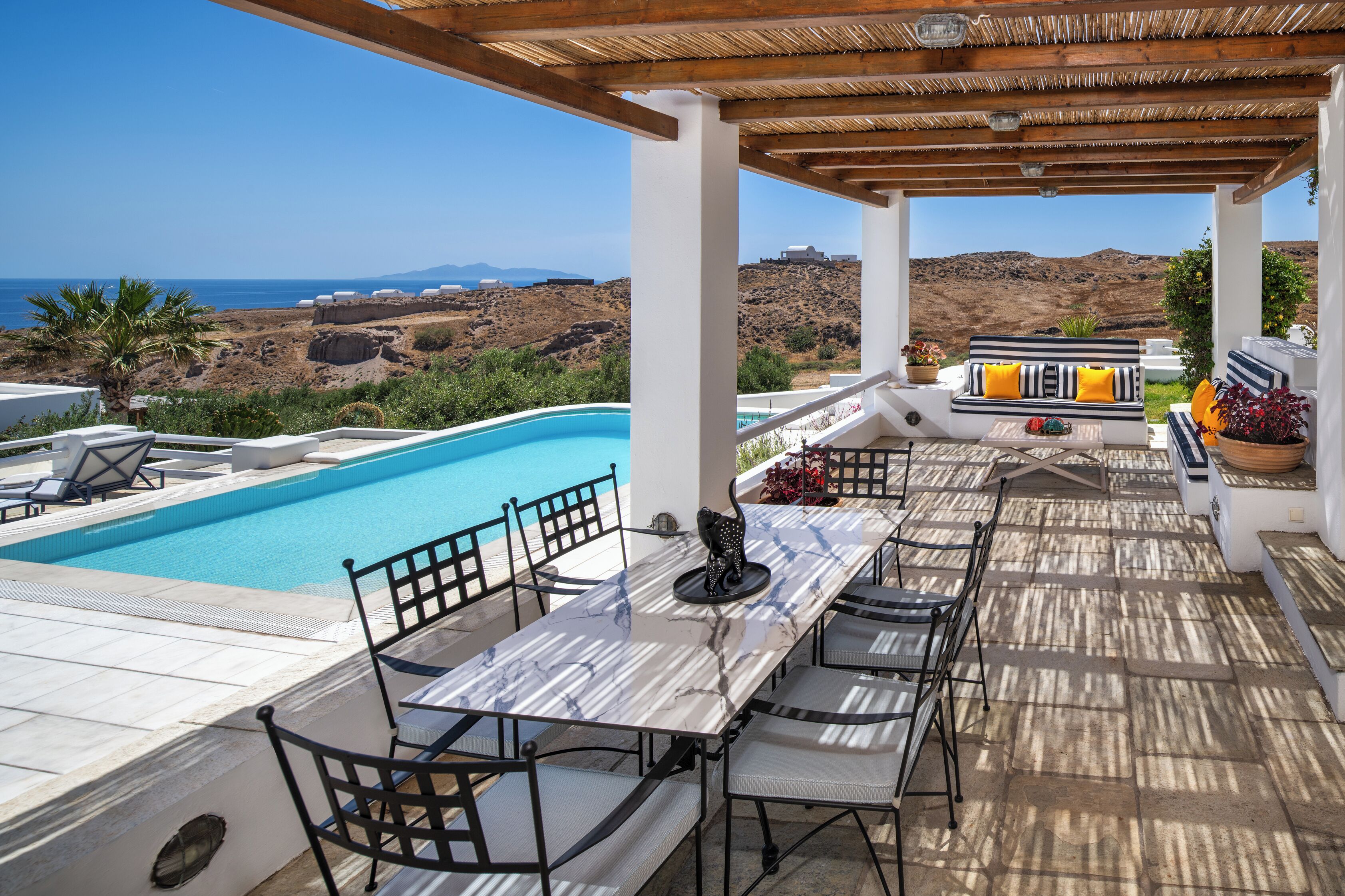A covered outdoor area with a pool, seating, and a view of the sea.