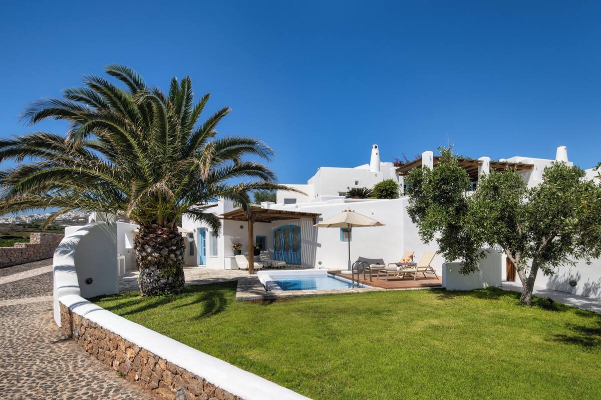 A white villa with a swimming pool, palm trees, and a clear blue sky.