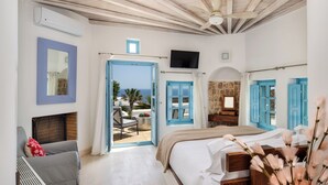 Een slaapkamer met een bed, een stoel, een televisie en uitzicht op zee.