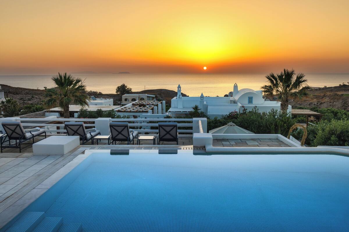 A rooftop infinity pool with lounge chairs and a view of the sunset over the sea.