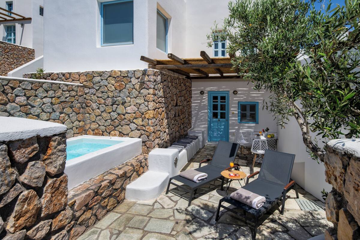A stone-walled outdoor area with a hot tub, lounge chairs, and a small table.