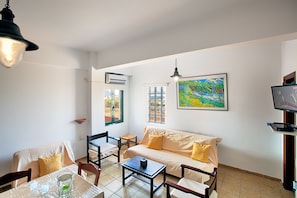 A living room with a sofa, chairs, a coffee table, a TV, and a painting on the wall.
