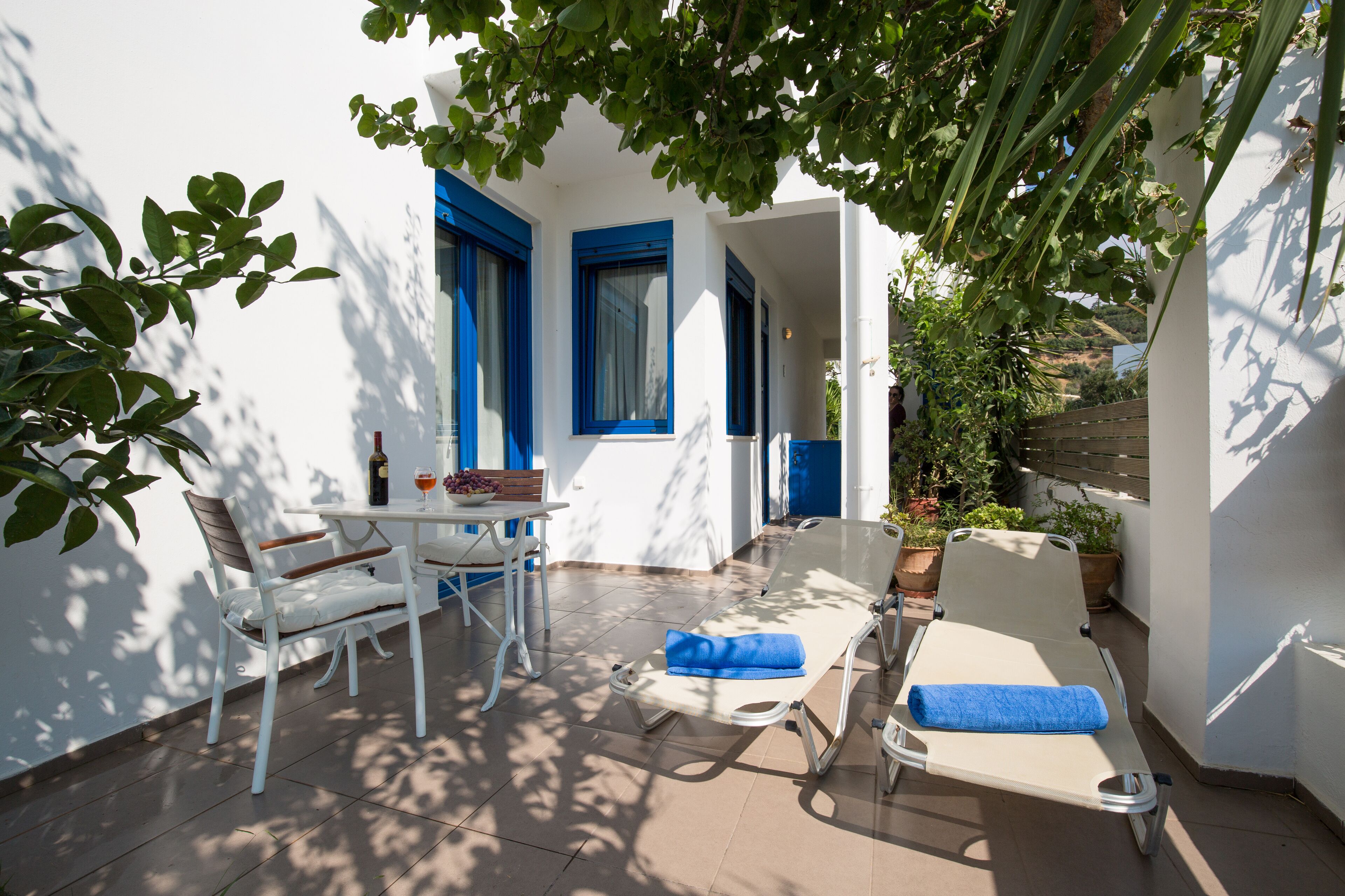 Un patio luminoso con un tavolo bianco, due sedie bianche, una poltrona con un asciugamano blu e una bottiglia di vino.
