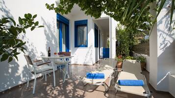 Un patio luminoso con un tavolo bianco, due sedie bianche, una poltrona con un asciugamano blu e una bottiglia di vino.