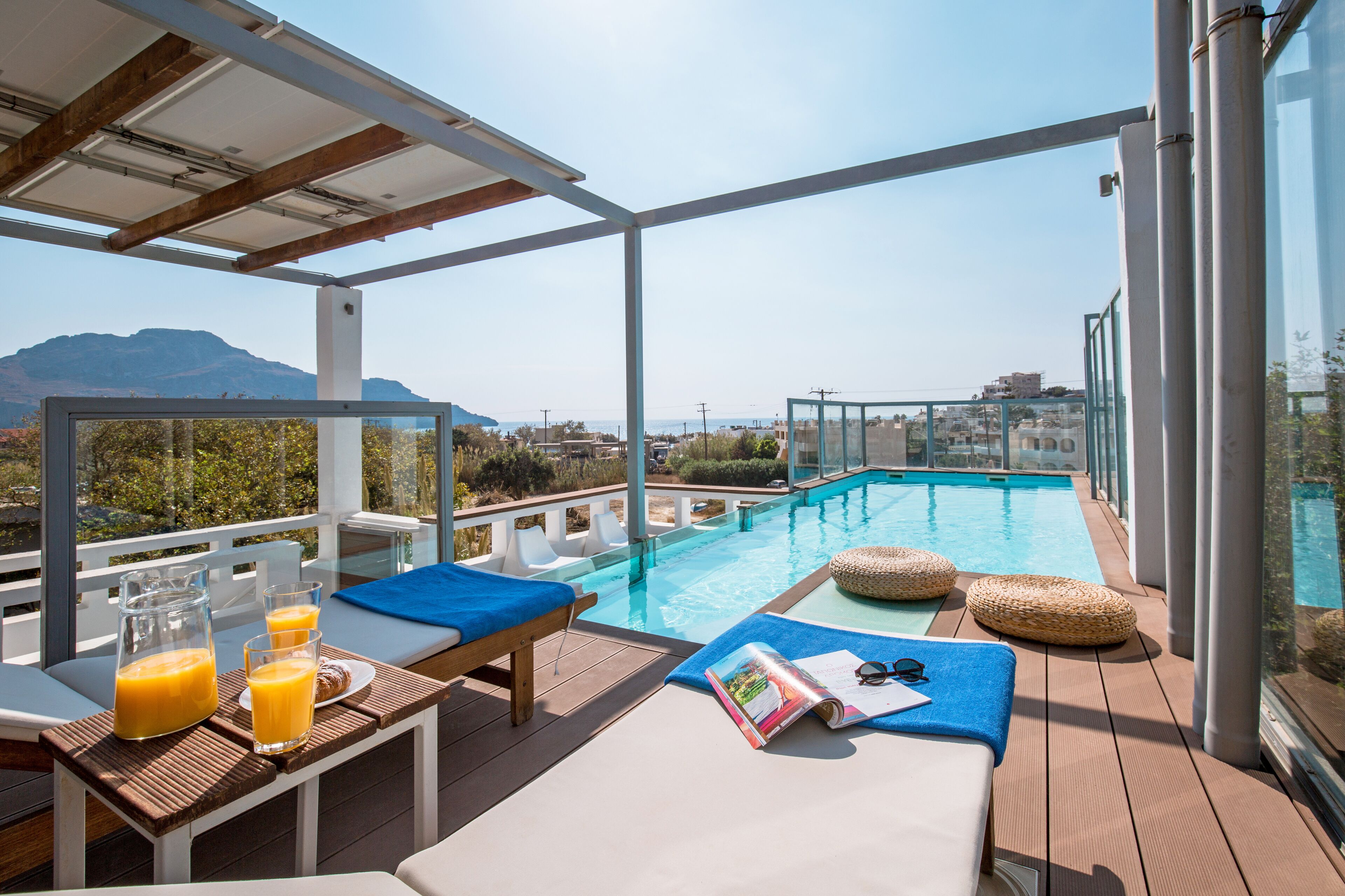 A rooftop pool area with lounge chairs, a table with drinks, and a magazine.