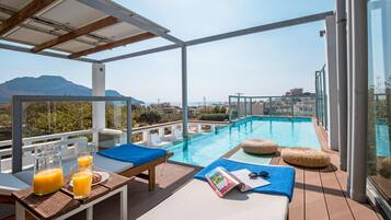 A rooftop pool area with lounge chairs, a table with drinks, and a magazine.
