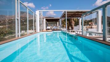 A modern infinity pool with clear blue water, surrounded by glass walls offering panoramic views of the landscape.