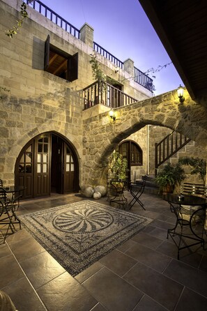 A courtyard with stone walls, arched doorways, and outdoor seating. - Camelot Traditional & Classic Hotel (Rhodes)