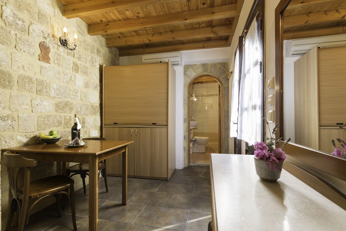 Une cuisine avec une table en bois, des chaises et un vase rempli de fleurs. On y trouve un mur en pierre et un plafond en bois.