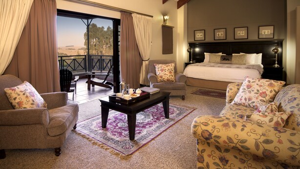 Amplia habitación con una cama grande, dos sillones, una mesita de centro y vistas al exterior a través de una puerta corredera.