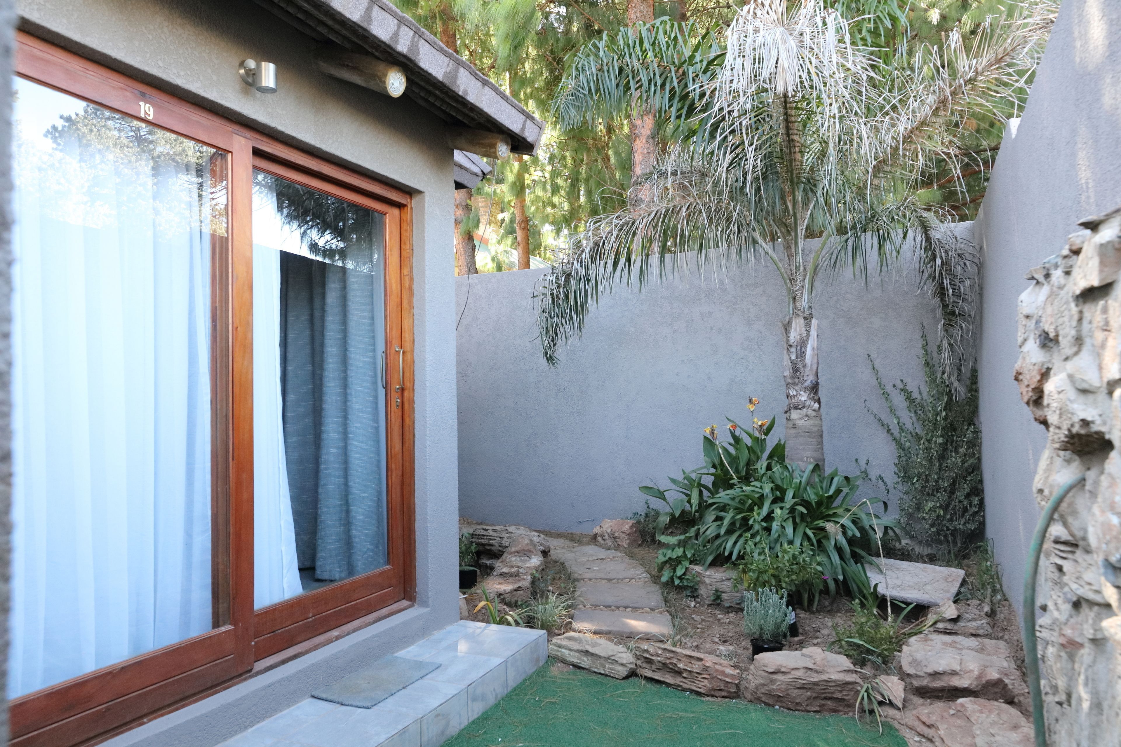 A modern house with a glass door, a stone pathway, and a small garden with various plants.