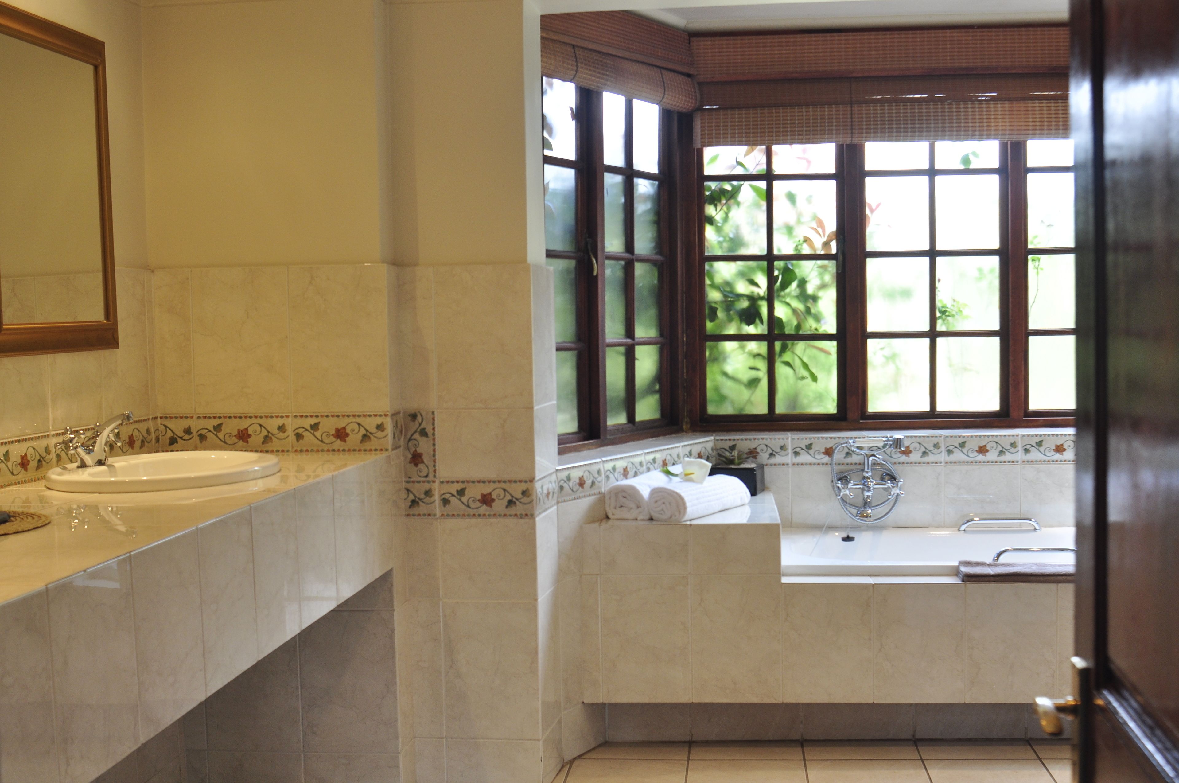 A bathroom with two sinks, a bathtub, and a window with a view of greenery.