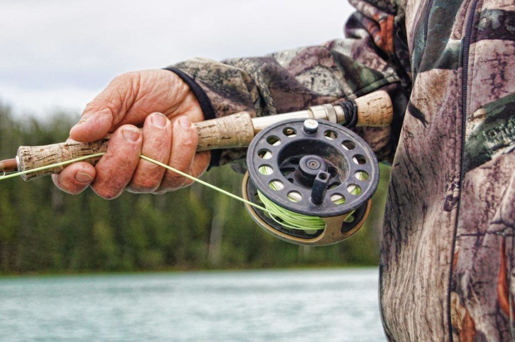 A person holding a fishing rod with a reel and line, wearing camouflage clothing.