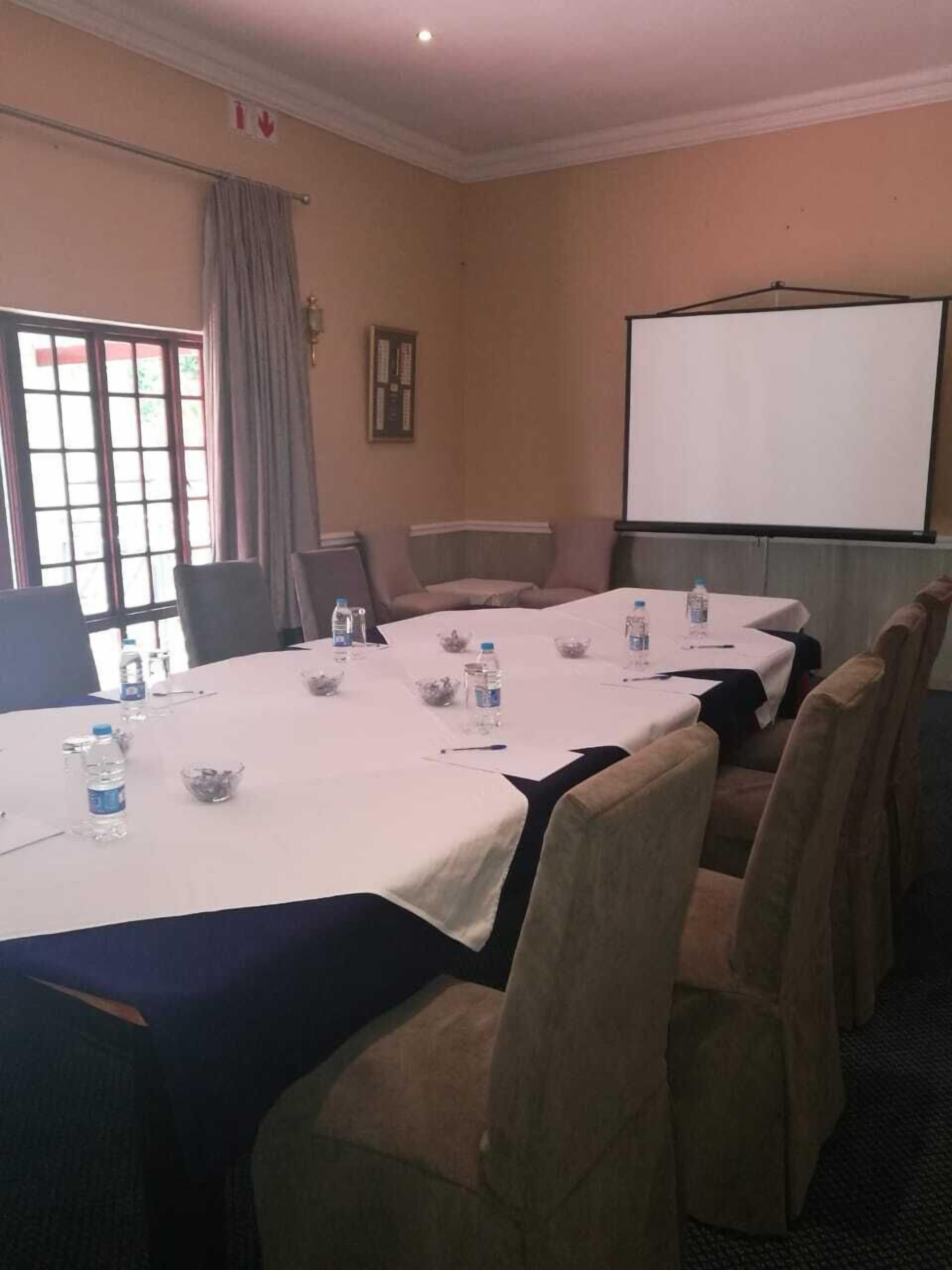 Une salle de conférence avec une longue table, des chaises, des bouteilles d’eau et un écran de projection.