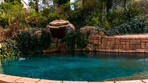 Una piscina con borde de piedra, rodeada de vegetación y rocas.