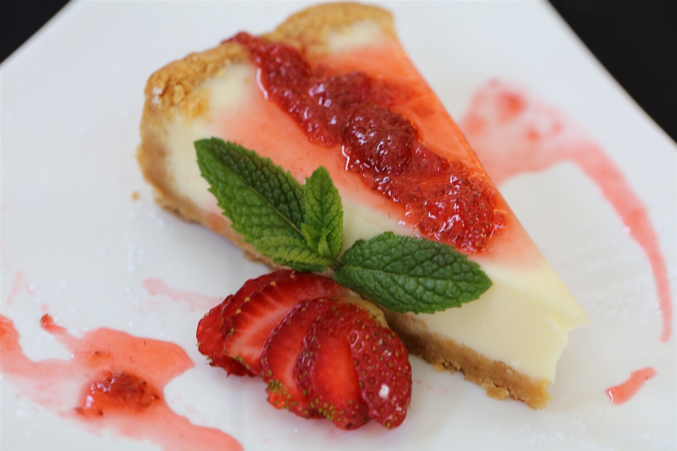 A slice of cheesecake with strawberry sauce and mint leaves.