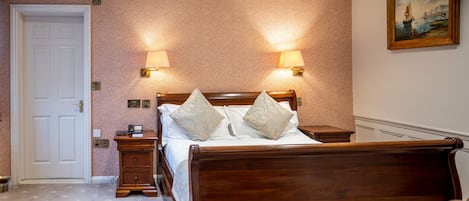 Quarto bem arrumado com cama de madeira, duas luminárias de cabeceira, mesa de cabeceira e uma porta.