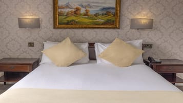 A hotel room with a large bed, two bedside tables, a painting on the wall, and two wall-mounted lamps.