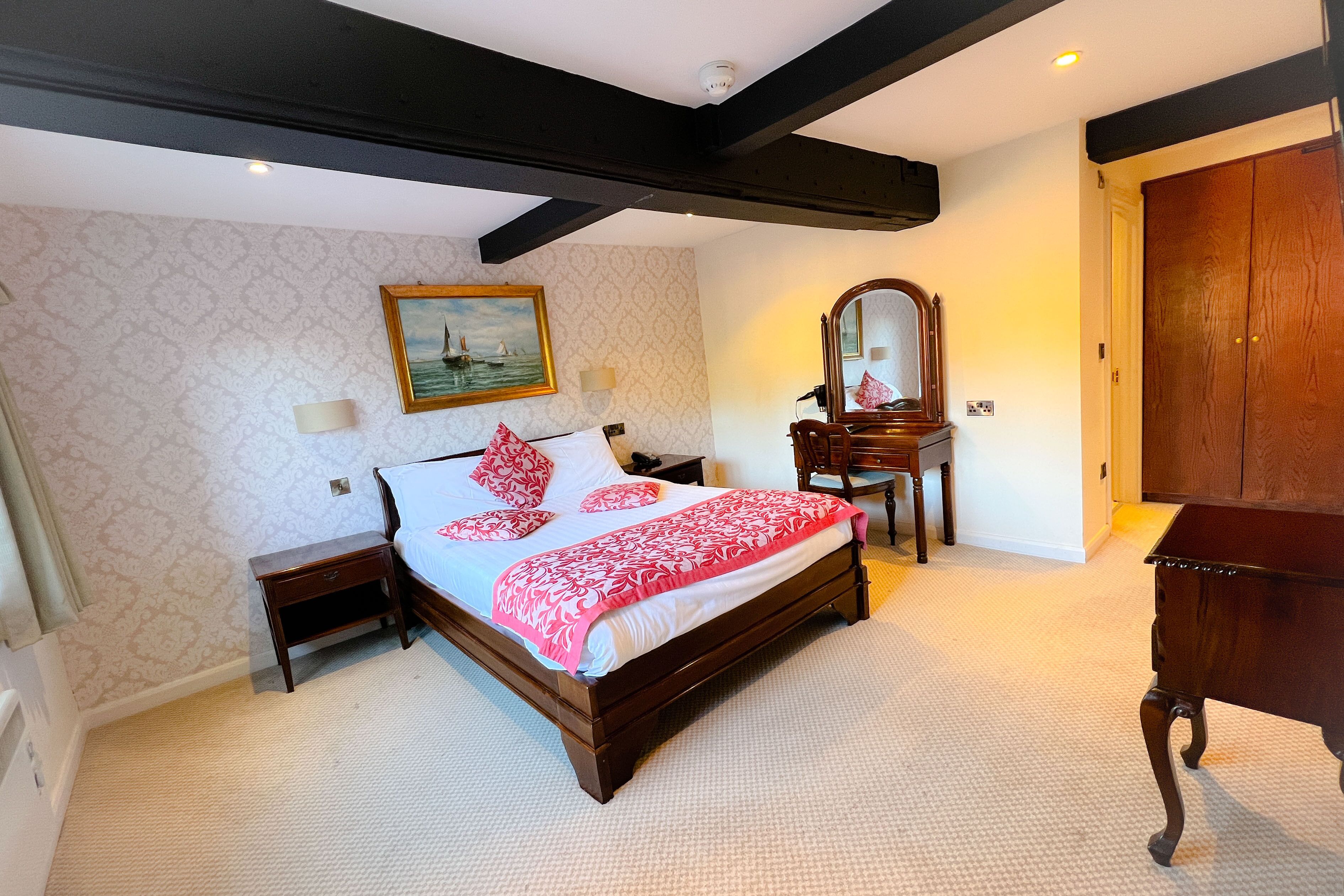 Ein Schlafzimmer mit einem großen Bett, einem Holzschrank, einem Schreibtisch, einem Spiegel und einem Bild an der Wand.
