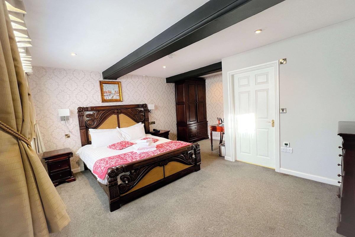 A bedroom with a large bed, a wooden headboard, a nightstand, a dresser, and a door.