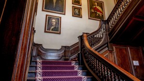 Un magnifique escalier orné de boiseries sculptées et une série de portraits encadrés qui décorent les murs.