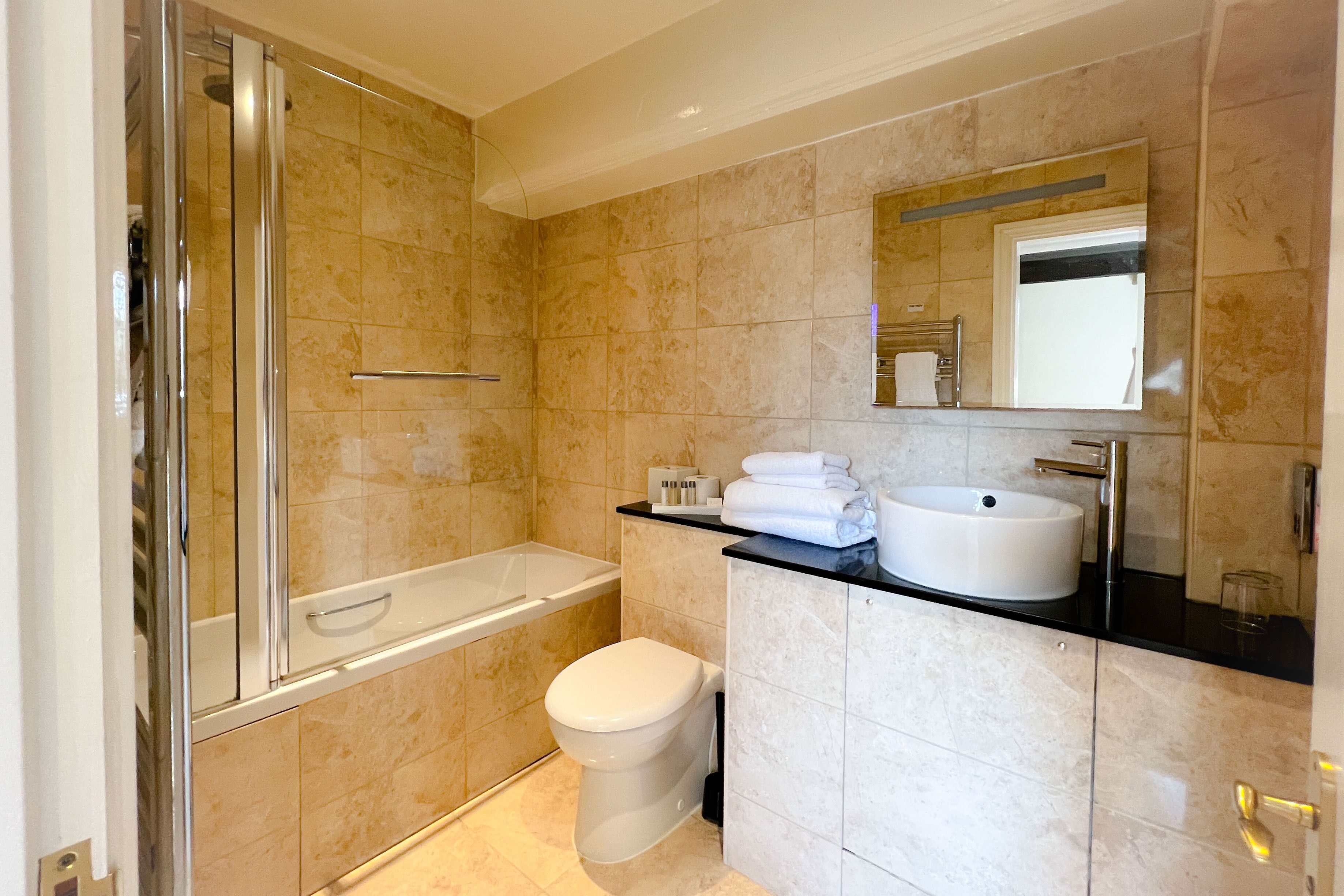 A modern bathroom with a glass-enclosed shower, a white toilet, a sink with a mirror, and beige tiled walls.