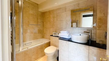 A modern bathroom with a glass-enclosed shower, a white toilet, a sink with a mirror, and beige tiled walls.