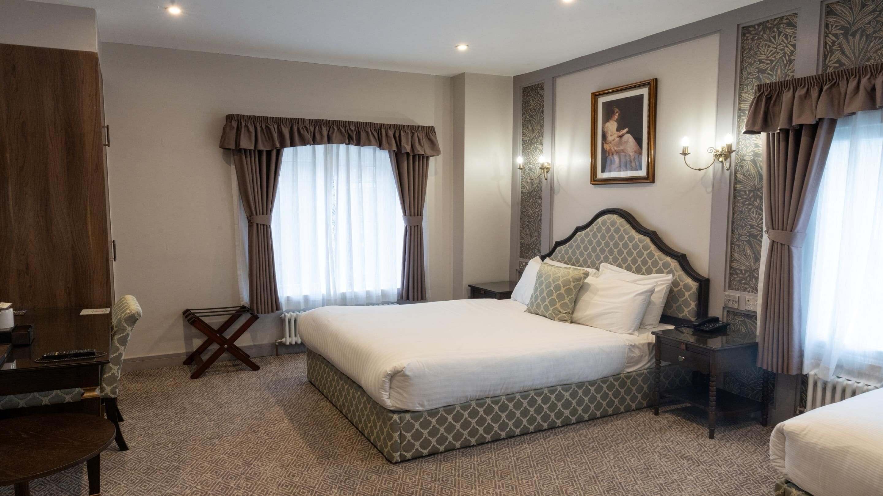 Habitación de hotel con una cama grande, un escritorio, una silla, un radiador y un cuadro en la pared.