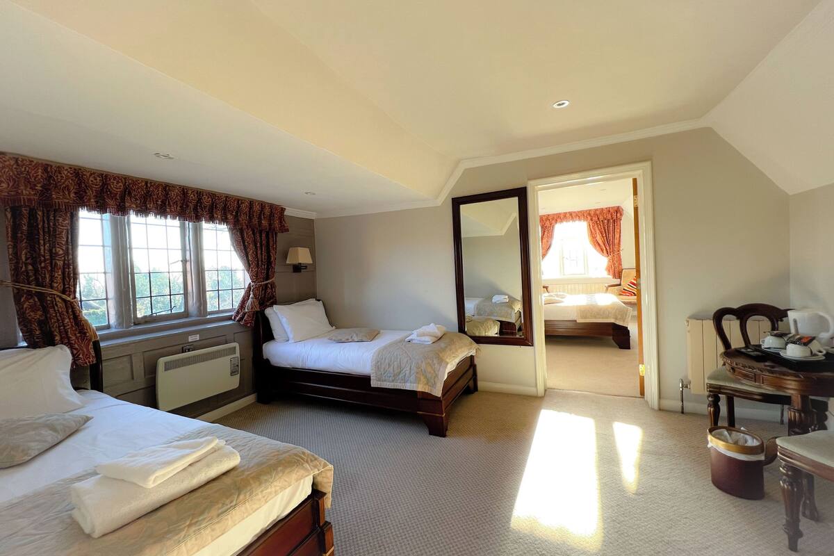 A hotel room with two beds, a large mirror, a dining table with chairs, and a view of the outside through the window.