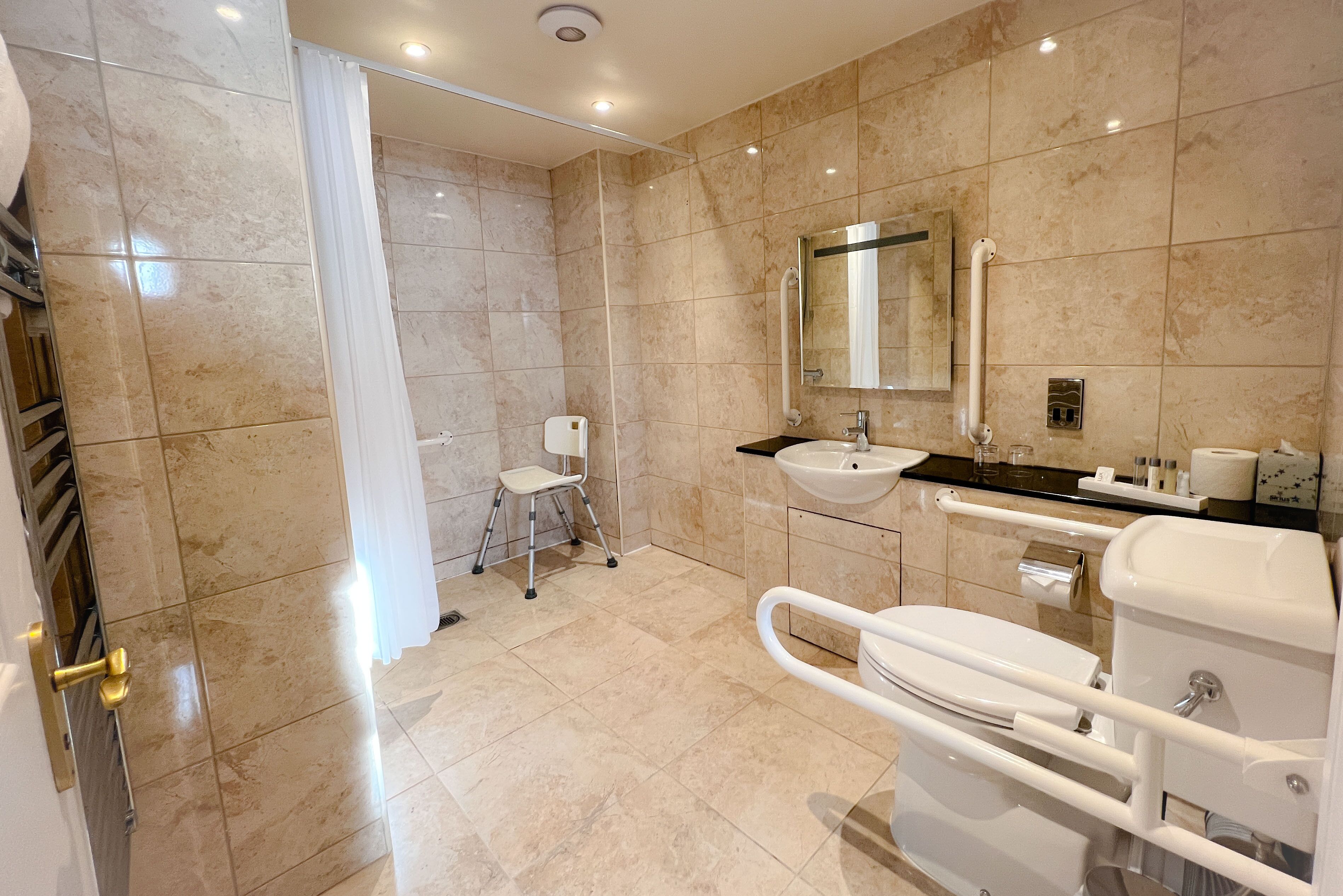 Un baño moderno con cabina de ducha, inodoro con barras de apoyo, lavabo y espejo.