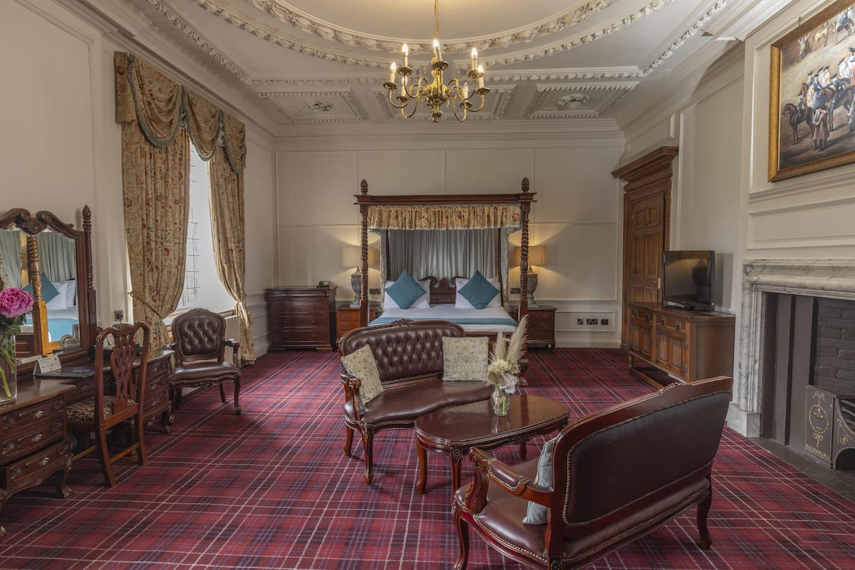 A room with a four-poster bed, a chandelier, and a fireplace.
