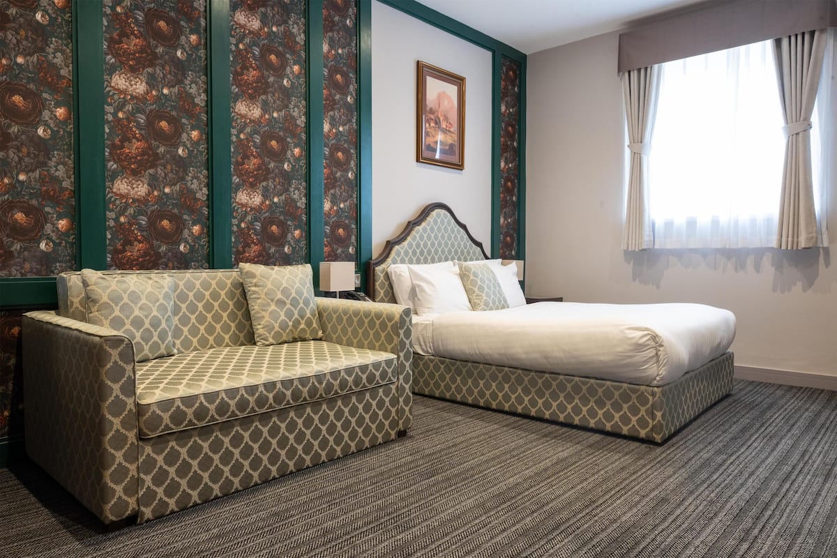 A hotel room with a bed, a sofa, a patterned wall, and a framed picture on the wall.