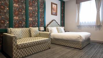 A hotel room with a bed, a sofa, a patterned wall, and a framed picture on the wall.