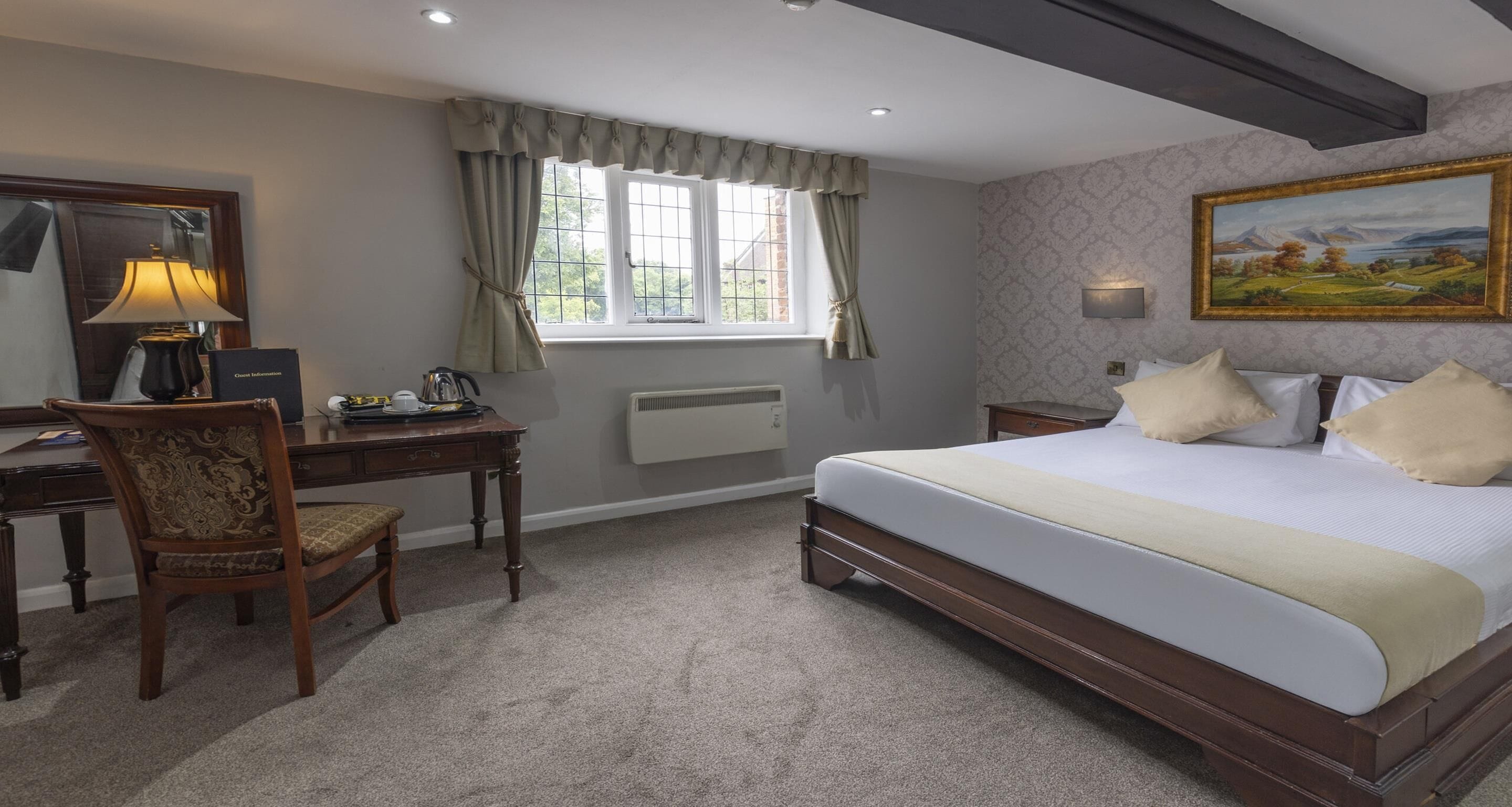 A bedroom with a bed, a desk, a chair, a window with curtains, a radiator, and a painting on the wall.