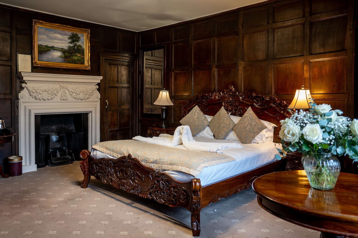 A classic bedroom with a large bed, a fireplace, and a wooden panel wall.