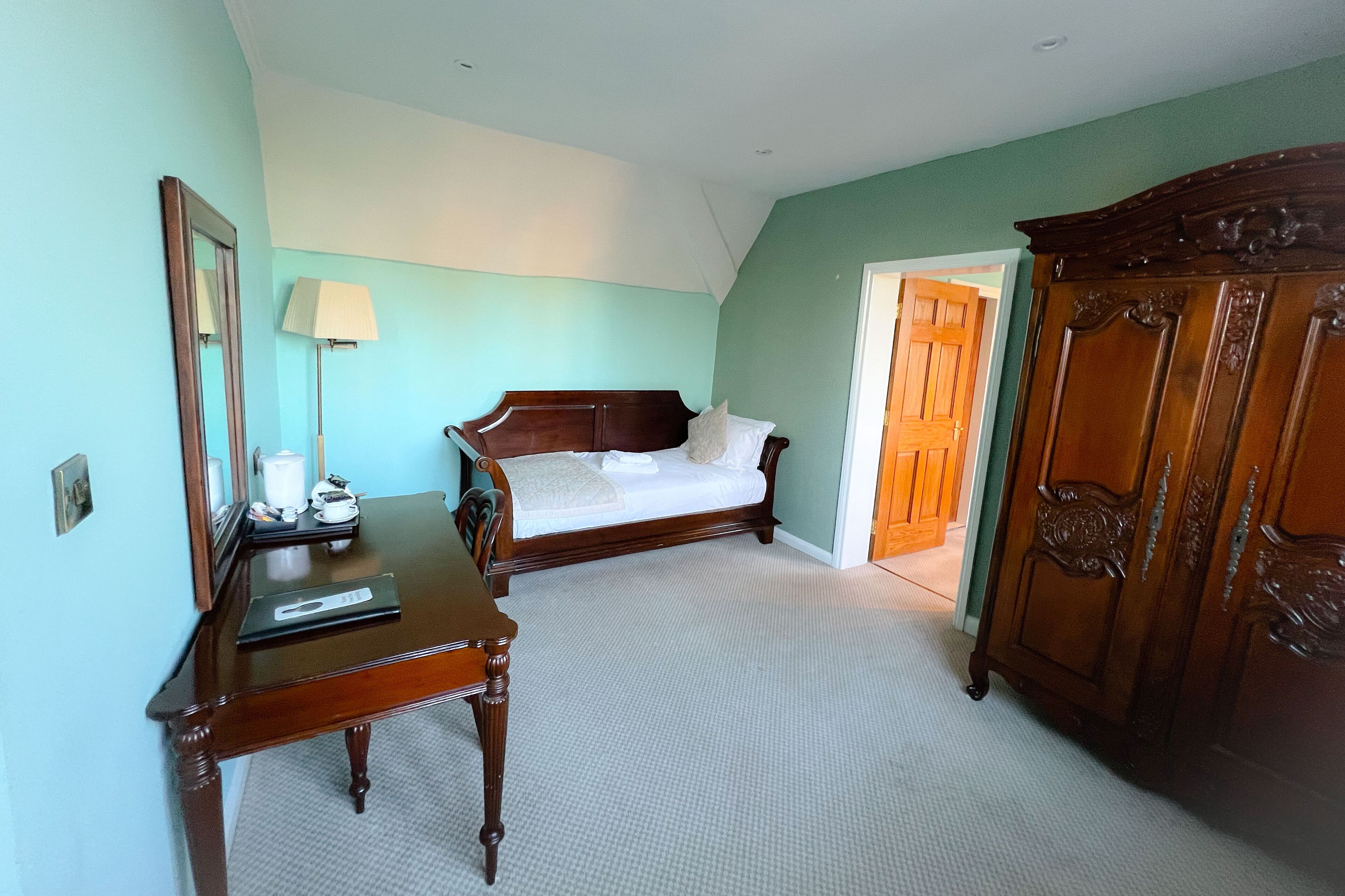 Une chambre à coucher avec un lit, une commode en bois, un bureau avec une lampe et un miroir.