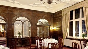 Une salle à manger élégante, ornée de boiseries sculptées, de grandes fenêtres en arc de cercle et de lustres.
