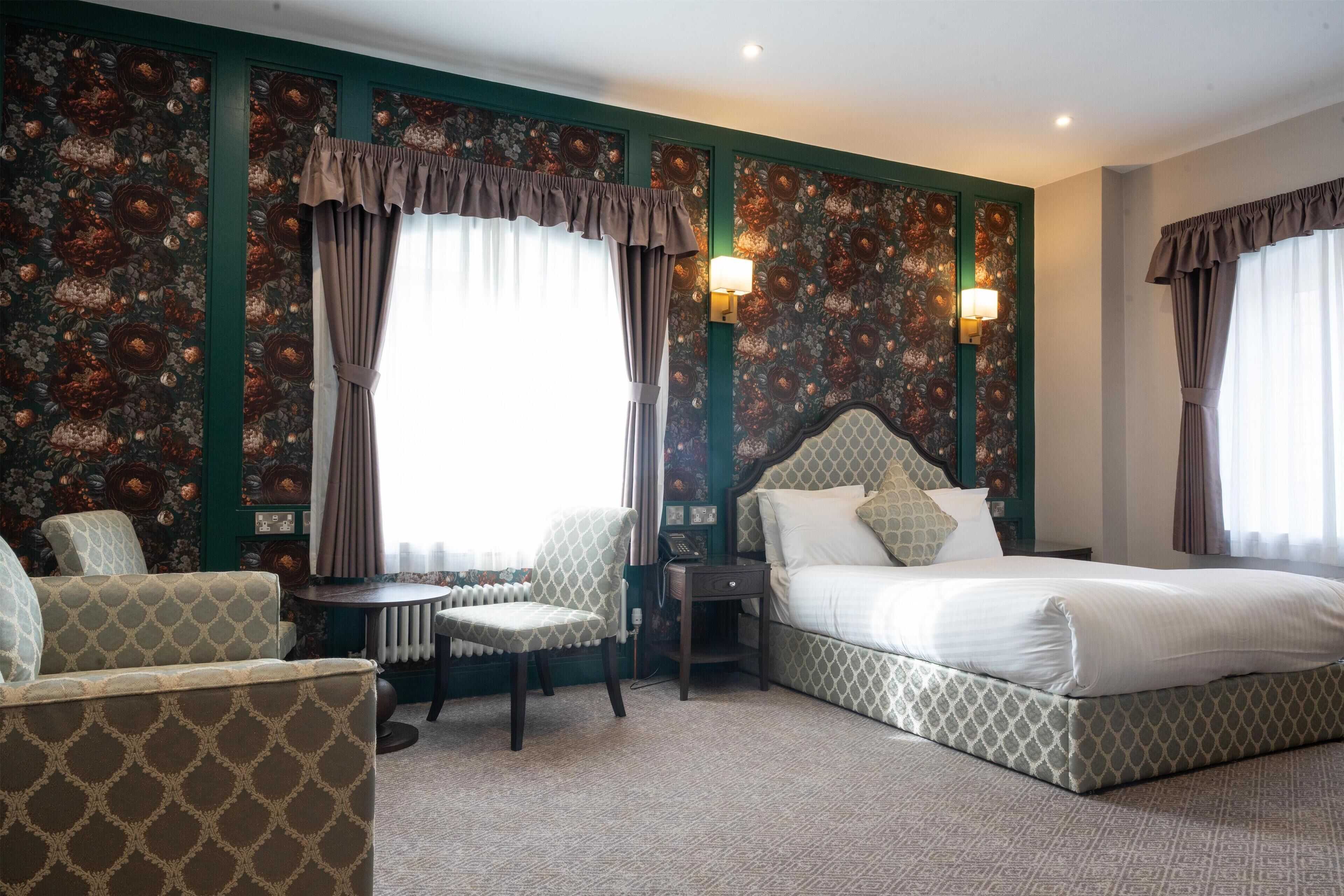 Une chambre d’hôtel avec un lit, deux fauteuils, une petite table et un radiateur.