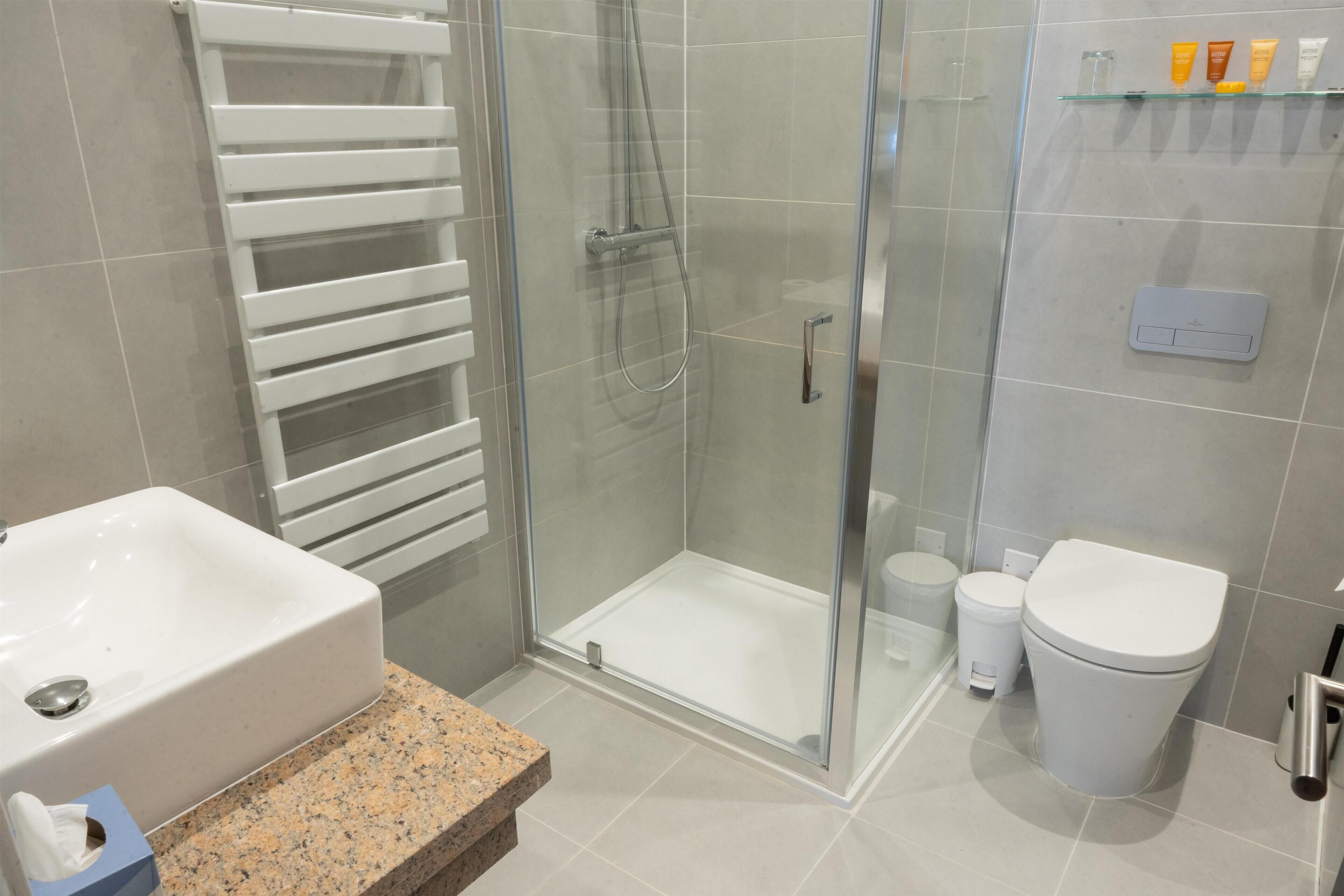 Un baño moderno con ducha de vidrio, un lavabo blanco y un inodoro.