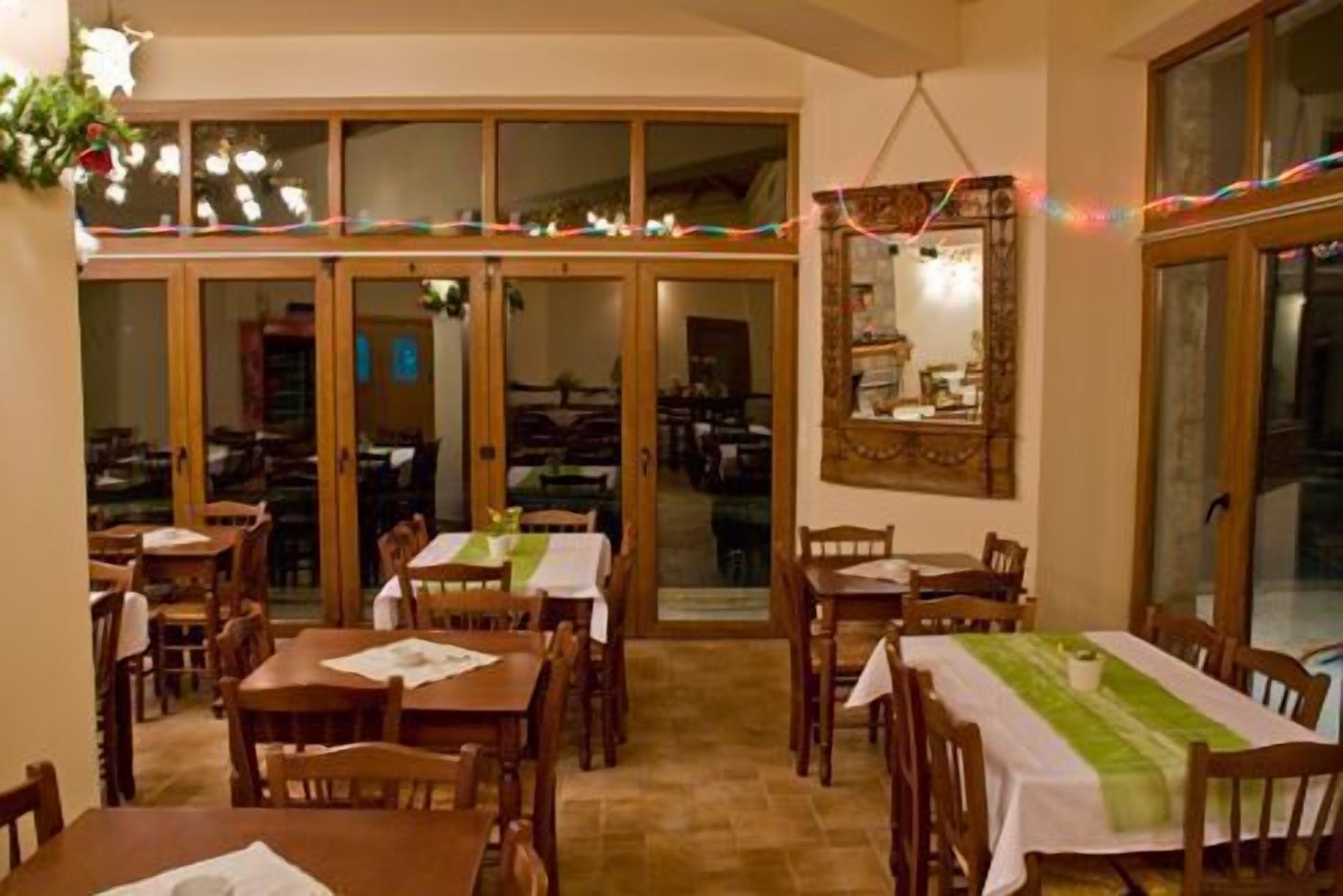 Zona pranzo con tavoli e sedie in legno, un'ampia finestra con tende e uno specchio a parete.