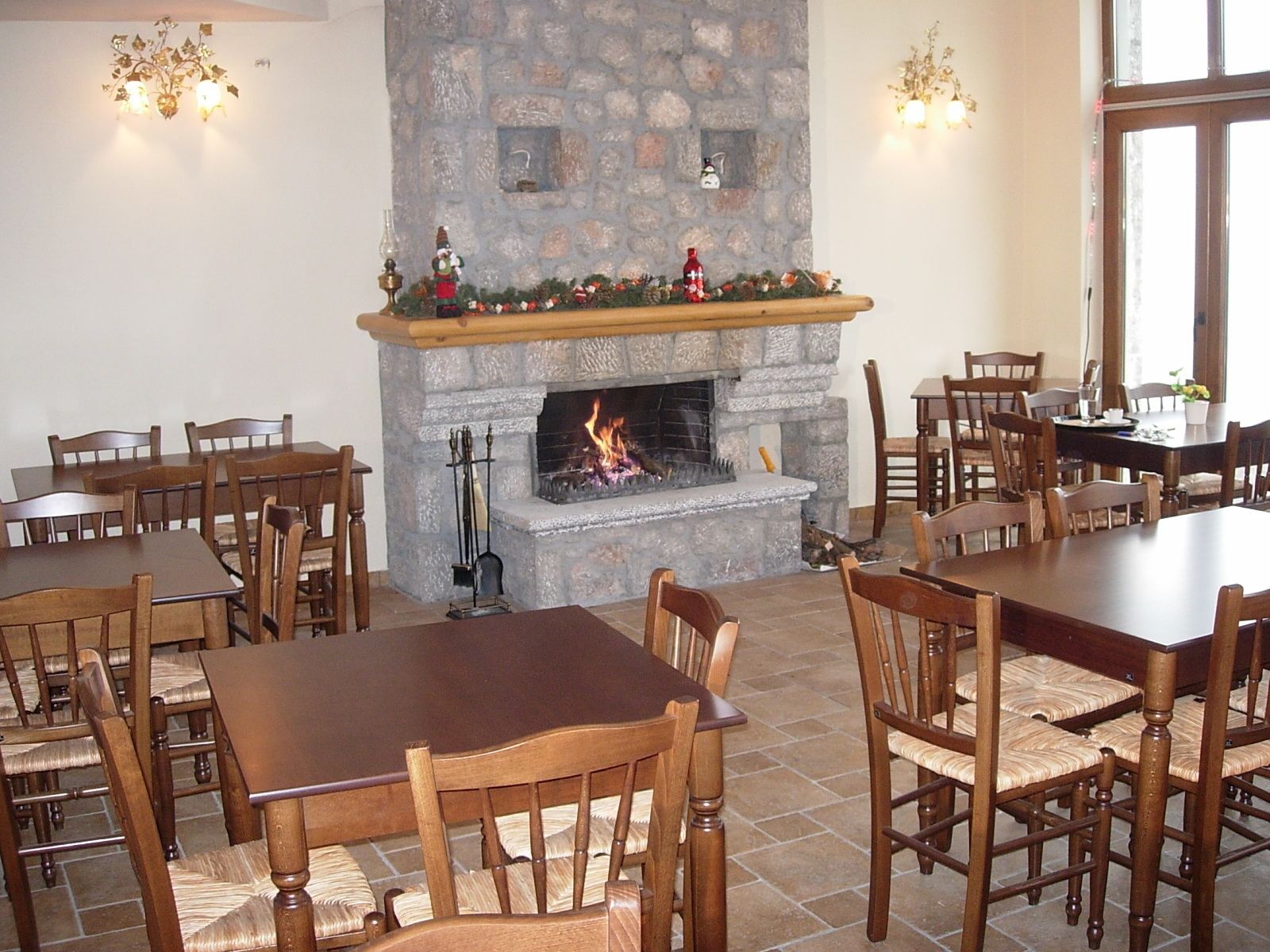 A dining area with stone fireplace, wooden tables and chairs, and wall-mounted lighting.