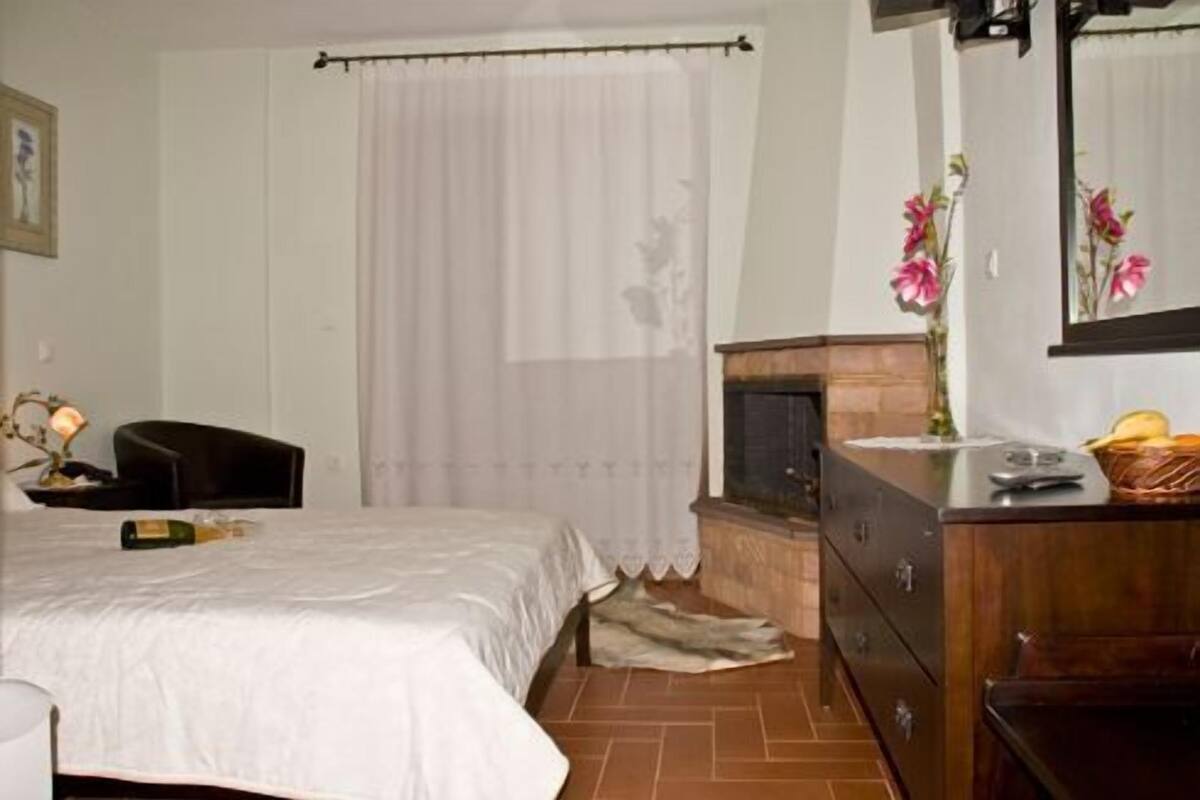 Ein Schlafzimmer mit Bett, Schminktisch, Nachttisch, Lampe und einem Fenster mit Vorhängen.