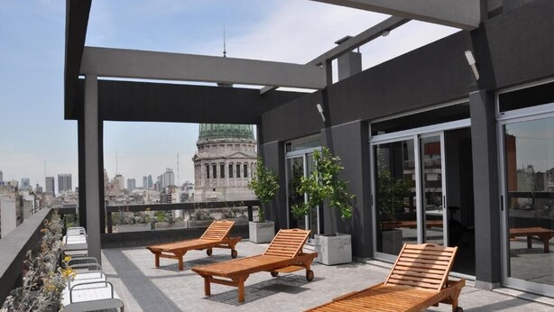 Terraza en la azotea con tumbonas, plantas en macetas y vistas a la ciudad.