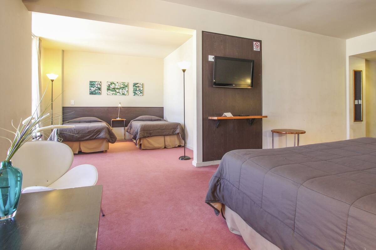 A hotel room with a large bed, two bedside tables, a TV mounted on the wall, and a small desk with a chair.